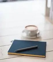 carnet noir avec un crayon et une tasse à café pour démontrer les outils et services de gestion de condo offerts par les gestionnaires de copropriété à Montréal